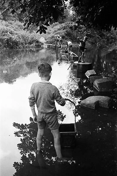 Young boys playing on some stepping stones on a river in Surrey. Circa 1945