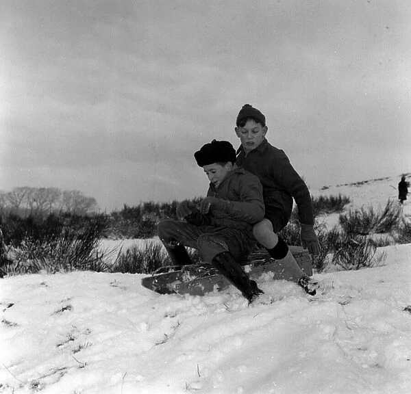 Two young boys riding their sledge down a snow covered hill January 1960