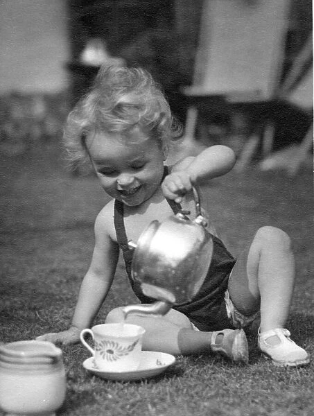 Young child pouring a cup of tea using a kettle in the back garden Circa 1945