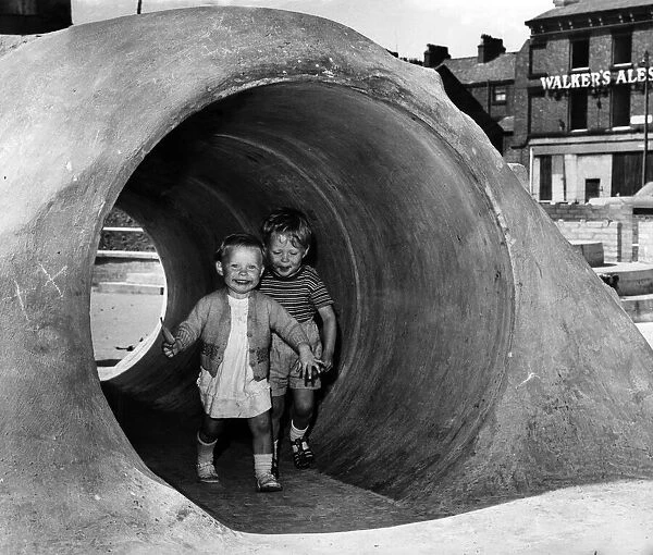 Two young children having fun running through a concrete tunnel in an adventure