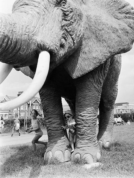 Young children playing between the legs of a model elephant statue at an adventure