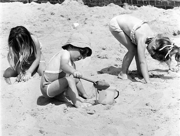 Young children playing in the sand, building sandcastles with a bucket