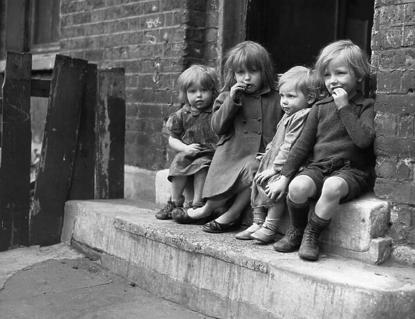 Young children sitting on the doorstep of one of their homes Doris Street, London