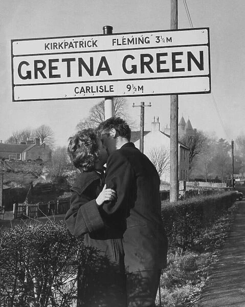 A young couple kissing under the Gretna Green Road sign