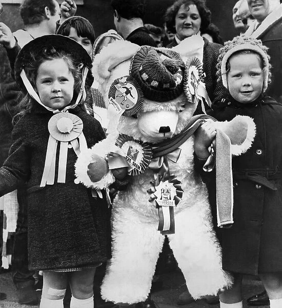 Young female fans of Skelmersdale Football club holding a giant mascot teddy bear as they