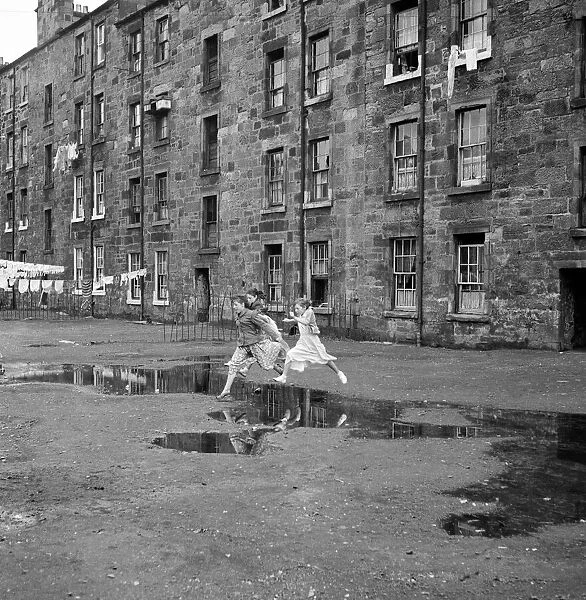Three young friends leap over a puddle outside a Govan tenement block in Glasgow