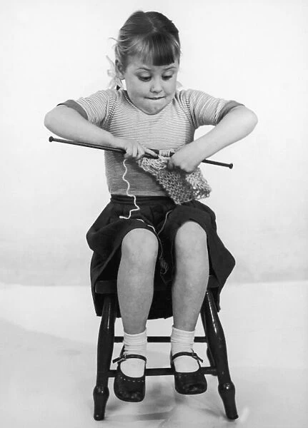 A young girl concentrating on her knitting, biting her lip sticking her elbows well out