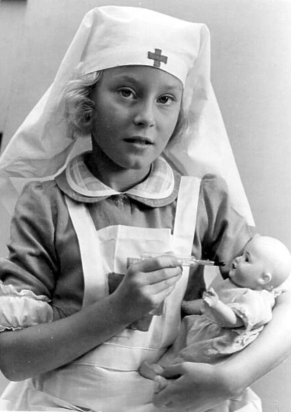 Young girl dressed in nurses outfit feeding her baby doll Circa 1945 P044506