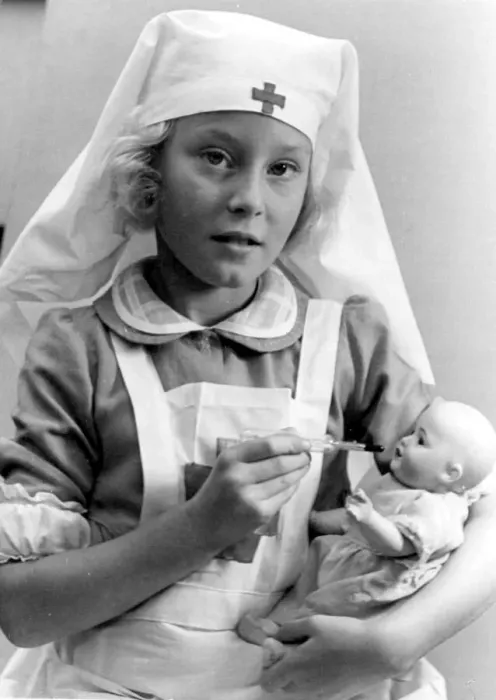 Framed Print : Young girl dressed in nurses outfit feeding her baby doll Circa 1945 P044506