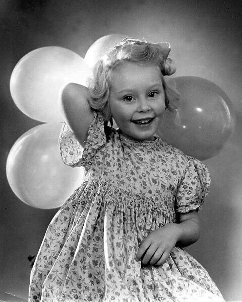 Young girl holding balloons for a party wearing floral patterned dress Circa 1945