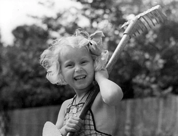 Young girl holding a rake in the back garden Circa 1945 P044440