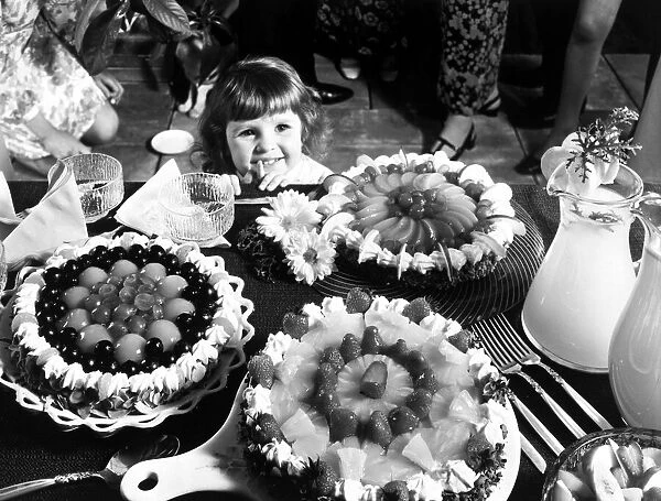 A young girl looking at a table with cakes Circa 1970