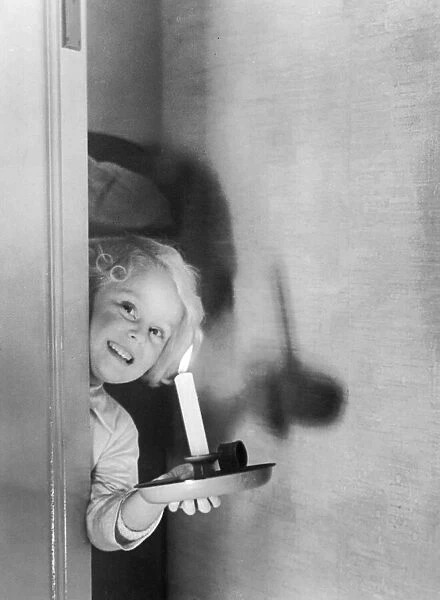 Young girl peering behind a door holding a candle Circa 1945 P044427