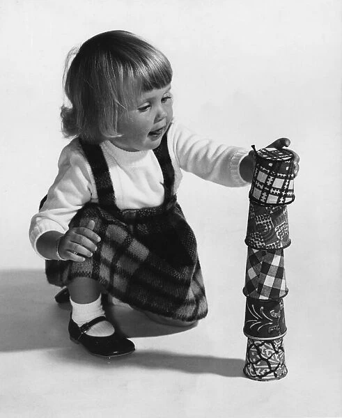 A young girl playing with a stack of cups. March 1964