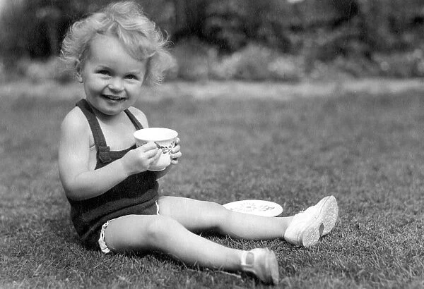 Young girl sitting in her back garden drinking from a cup Circa 1945 P044434