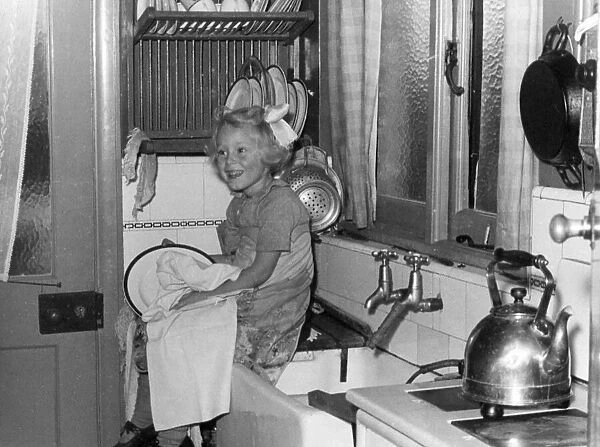 Young girl sitting on the kitchen worktop drying dishes after doing the washing up