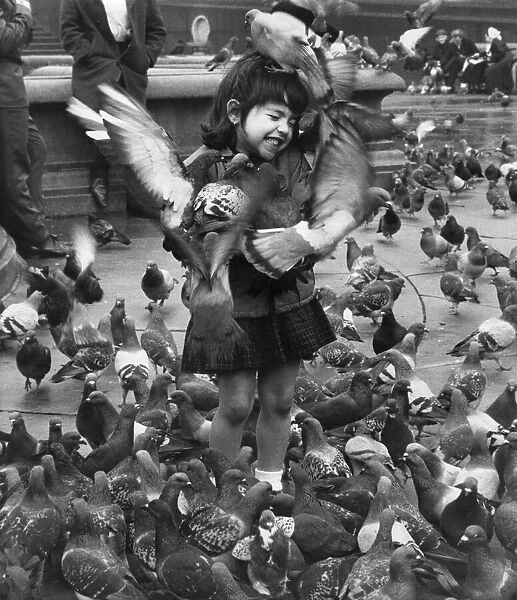 Young girl surrounded by hungry pigeons as she feeds them in Trafalgar Square