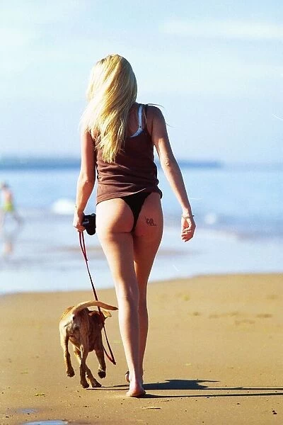 A young girl walk her dog in the sunshine on the beach at Whitley Bay