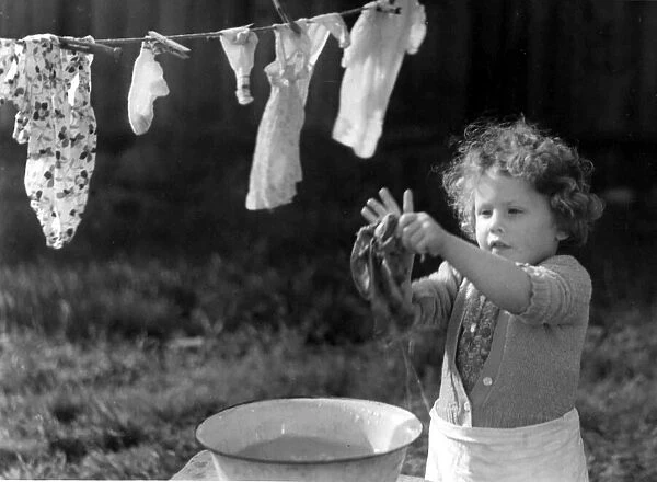 Young girl washing her clothes in a bowl of water and hanging them out to dry