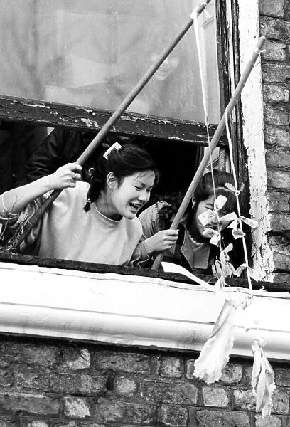 Young girls in Chinatown leaning out of a window, enjoying Chinese New Year celebrations