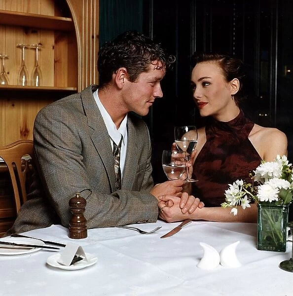Young man and woman holding hands at dinner table looking into each others eyes