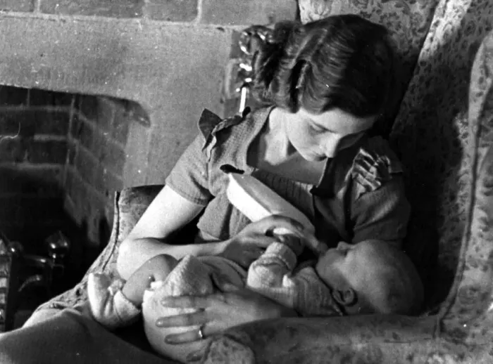 Framed Print : Young mother feeding her baby with a bottle of milk beside the fireplace Circa 1945