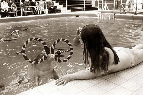 A young woman plays with a dolphin who is wearing comic glasses
