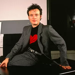 Adam Ant pop singer sitting on desk January 1990 Striped suit black jumper red