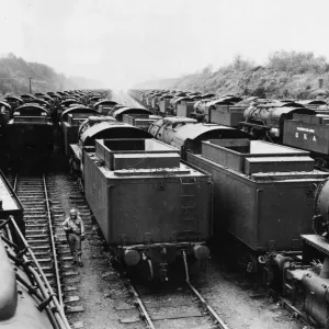 An American soldier stands on guard, surrounded American built locomotives at a rail An American soldier stands on guard, surrounded American built locomotives at a rail