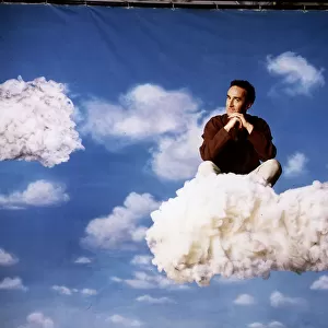 Angus Deayton TV presenter sitting on cloud in sky background back drop