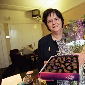 Ann Widdecombe in her Perliament office holding flowers and a box of chocolates