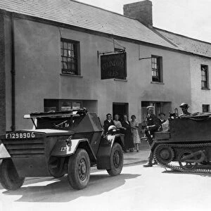 Armoured vehicles of the local Home Guard are flung across the High Street of a un-named