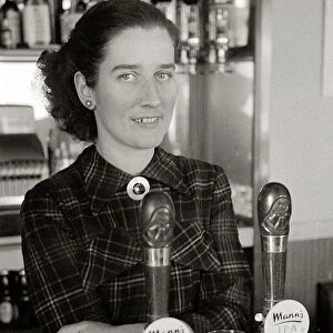 The barmaid at The Chimes Lansbury Public House stands behind the bar beside the beer