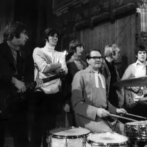 The Bee Gees pop group stand behind a vicar having a a go on the drums during rehearsals