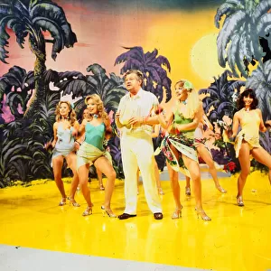 Benny Hill comedian 1989 With girls dancing on stage desert island palms trees set
