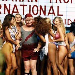 Benny Hill Comedian stands between bikini clad contestrants at a beauty competition