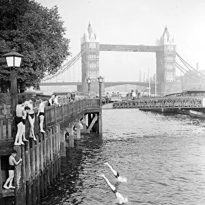 Boys jumping off the bank of the River Thames into the water on hot summers day near