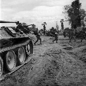 British infantry passing a knocked out German tank as they move up to consolidate a