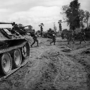 Britische Infanterie schreitet an einem ausgeschlagenen deutschen Panzer vorbei, während sie sich auf die Konsolidierung der Position bewegt