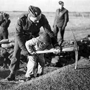 British troops in Iceland. A young child helping a soldier pickaxe the ground. Circa 1941