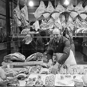Butcher standing in his shop window, showing off his various meat products currently