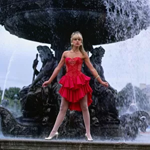 Carol Smillie model TV presenter wearing red dress standing ion front of a water fountain
