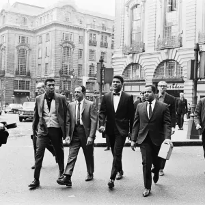 Cassius Clay (au centre) et son entourage au Piccadilly Circus en route vers sa conférence de presse. Cassius Clay (au centre) et son entourage au Piccadilly Circus en route vers sa conférence de presse.