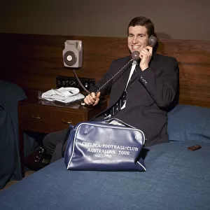 Chelsea footballer Peter Osgood on the telephone in his hotel room packing his bag