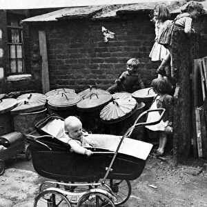 Children play amongst the rubbish bins in the back yard of their houses as a little baby