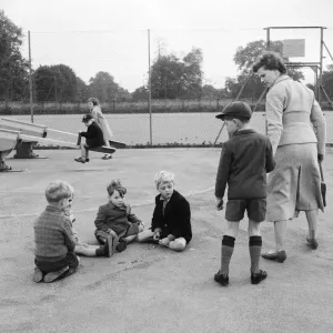 Children in the playground playing a game of marbles as one boy is dragged away by his