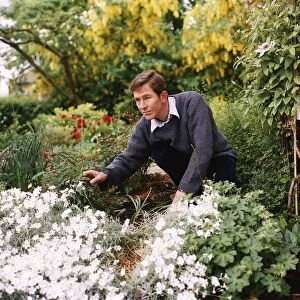 Christopher Ravenscroft Actor crouching down in his garden looking at a rose bush