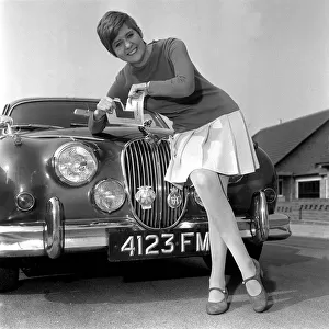 Cilla Black leaning on the grill of a Jaguar Car tearing up L