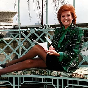 Cilla Black television presenter writing with feather legs streched along bench green