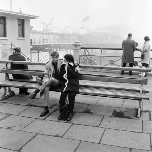 A couple dressed up and cuddled up to resist the cold on the Brighton front by the pier A couple dressed up and cuddled up to resist the cold on the Brighton front by the pier